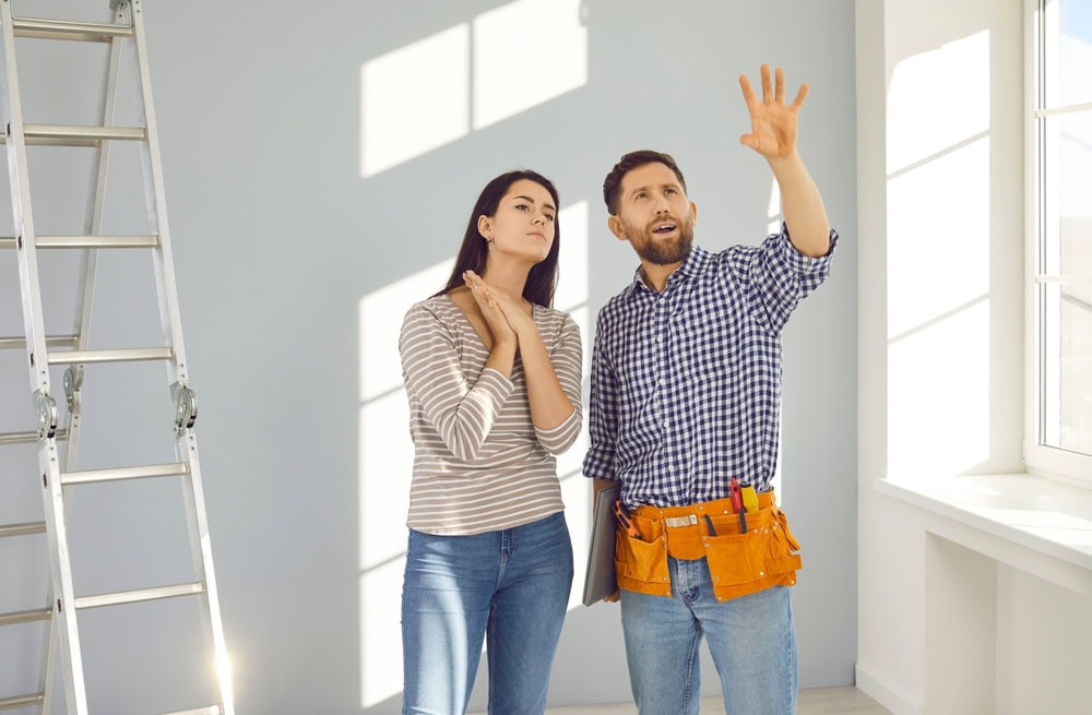 A confident contractor explaining home renovation plans to a woman in a bright, modern interior setting.