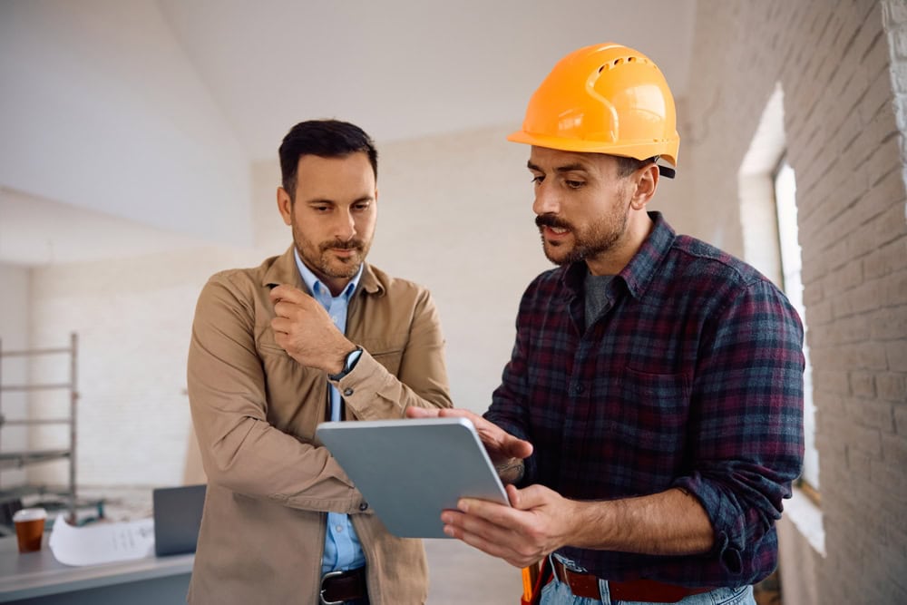 Construction worker reviewing project plans with supervisor in an unfinished building site at a construction company.