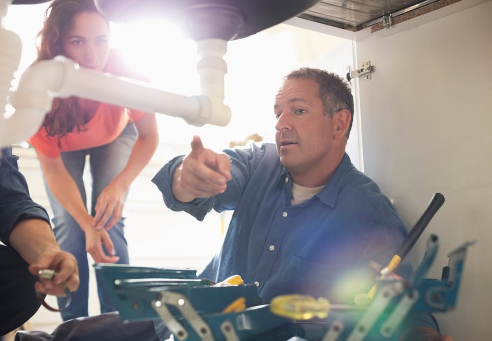 A licensed contractor explaining plumbing work to a woman during a consultation in a garage or workshop.