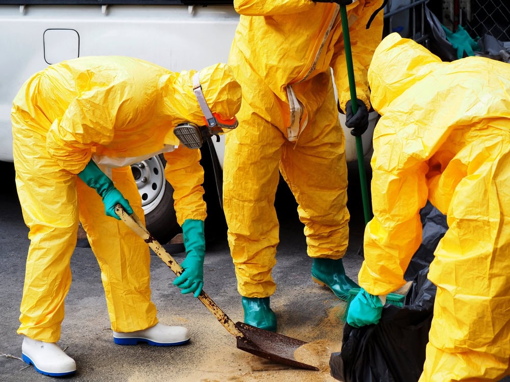 Hazmat cleanup workers in yellow protective suits collecting hazardous waste on street.