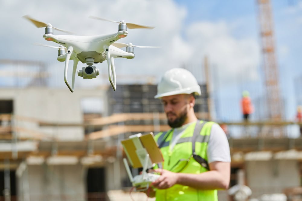 Drone flying over construction site with inspector using remote control and tablet on site.