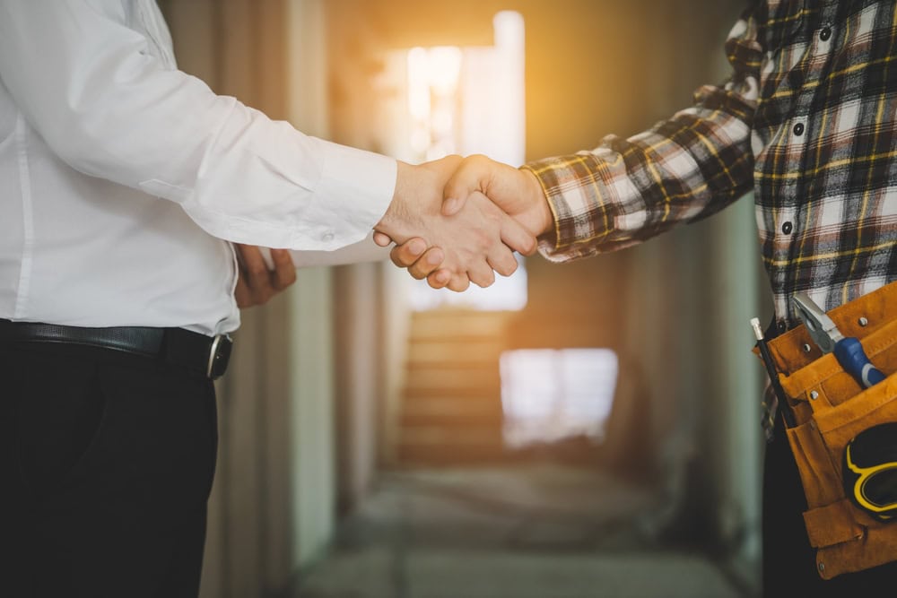 Two professionals shaking hands in a construction site, symbolizing contractor agreement and partnership.