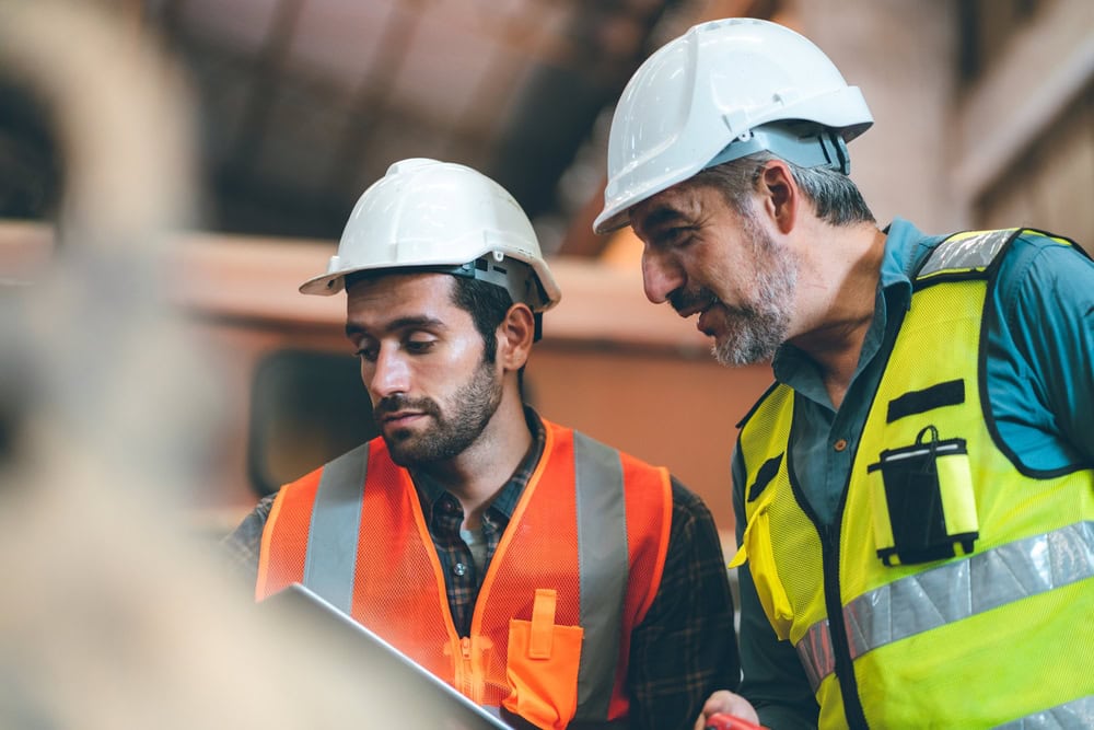 Hardhat-wearing construction professionals reviewing plans on-site for contractor licensing and project safety.