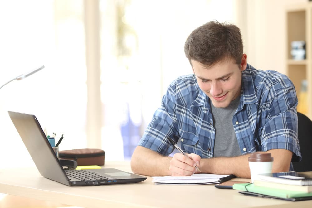 Young man studying with laptop and notepad for contractor licensing exam.