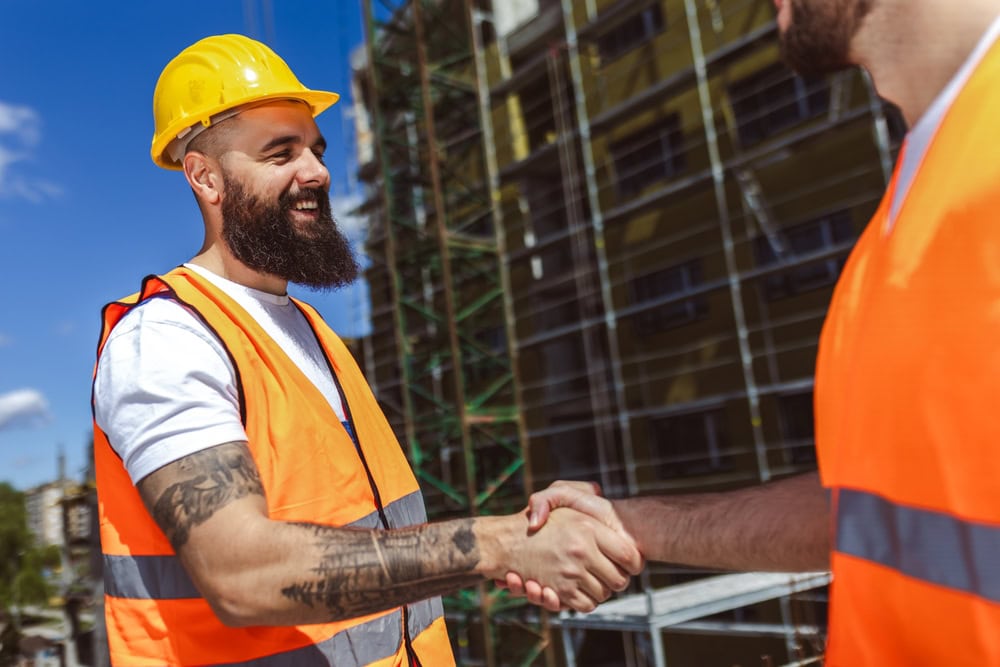 Hardhat construction workers shaking hands at a building site, symbolizing professionalism and successful partnerships in the contracting industry.