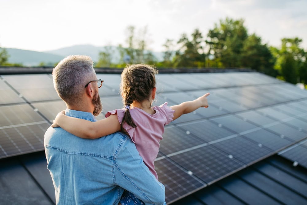 Solar panels on a rooftop, father and daughter pointing at the solar array, sustainable energy, clean energy, renewable power, eco-friendly home, family enjoying green energy, environmental conservation, alternative energy sources.