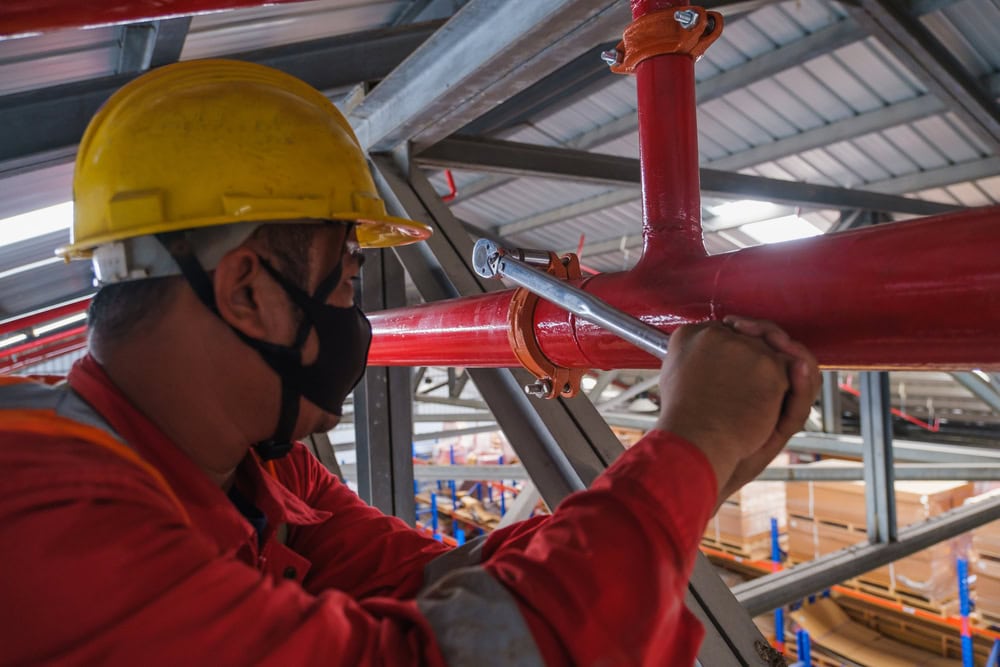 Welding worker inspecting a red pipe in an industrial facility under a metal roof construction site.
