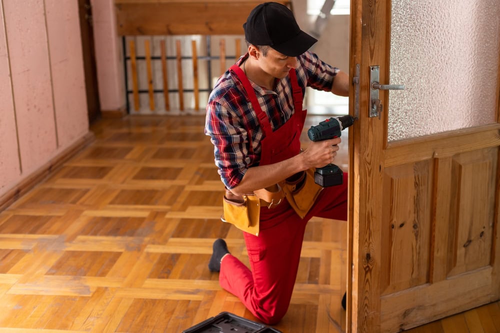 A handyman installing a wooden door with a cordless drill in a home interior.