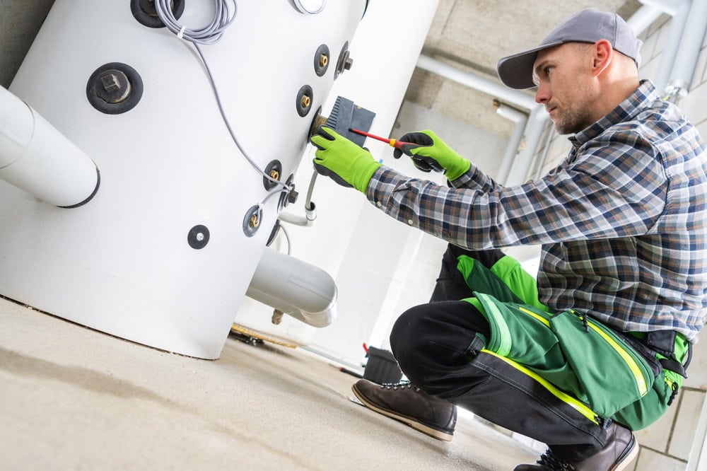 Professional technician inspecting water heater with tools at plumbing installation site.