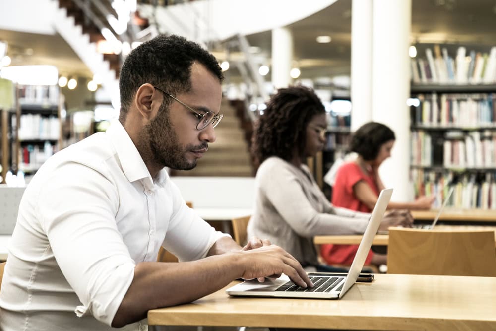 Responsive, diverse students studying on laptops in a bright library environment for contractor license education and certification.