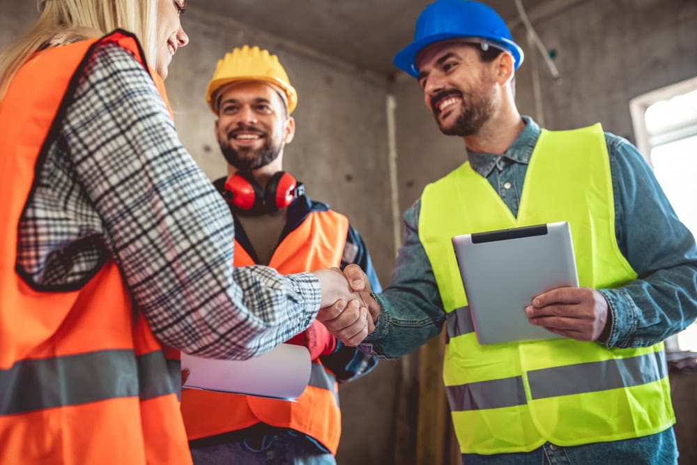 Construction workers shaking hands in a building site, representing contractor licensing and professional acknowledgment.