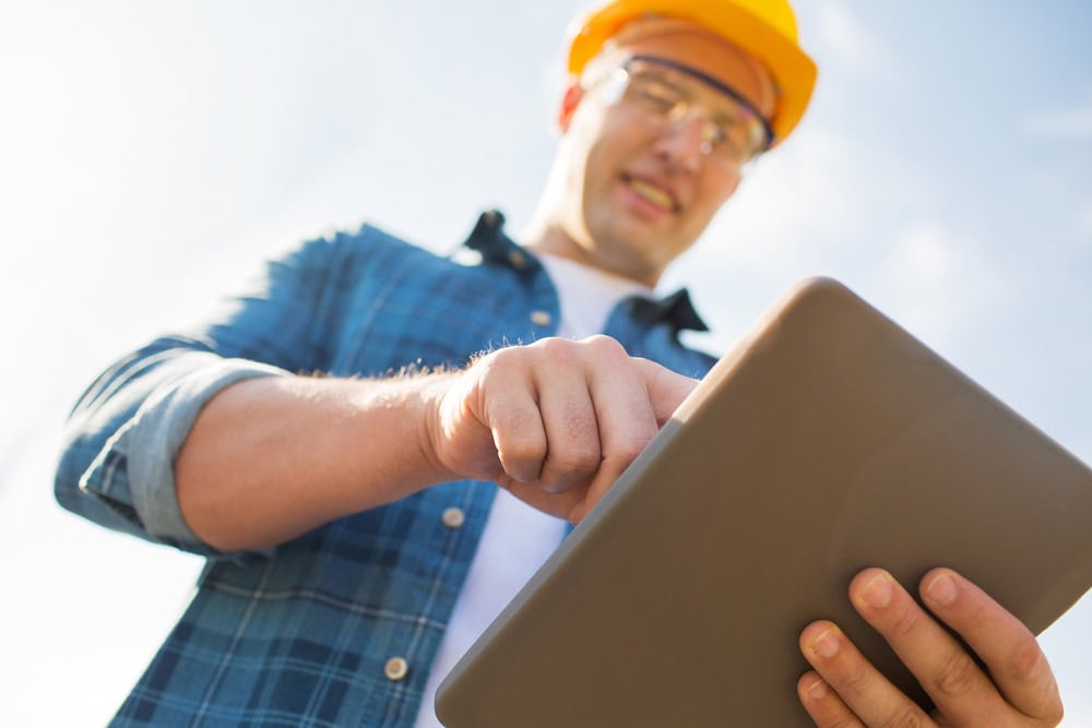 Men in construction helmet using tablet outdoors for contractor licensing information.