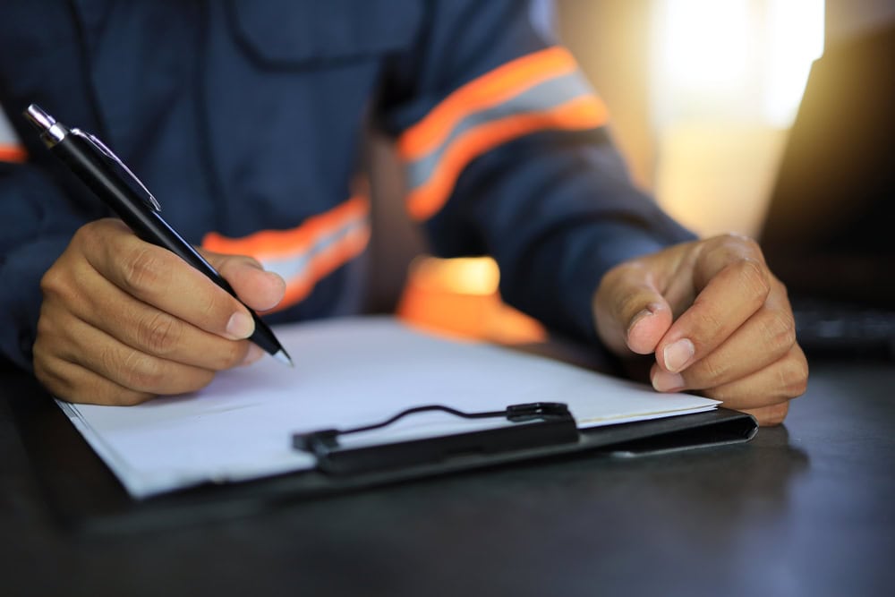 Hands holding a pen and filling out a form at a desk in workwear, on a construction site or office, in focus, professional contractor documentation.