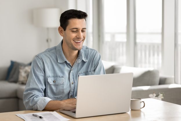 Licensed contractor smiling while working on a laptop in a bright, modern home office.