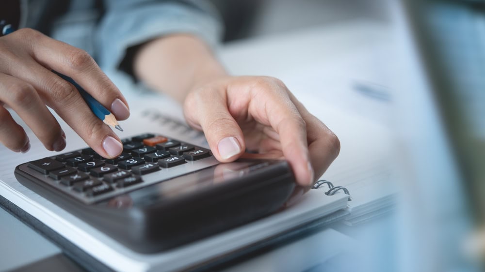 Visually focused on a person using a calculator and working with documents, likely related to contractor licensing; suitable for emphasizing financial planning or licensing steps.