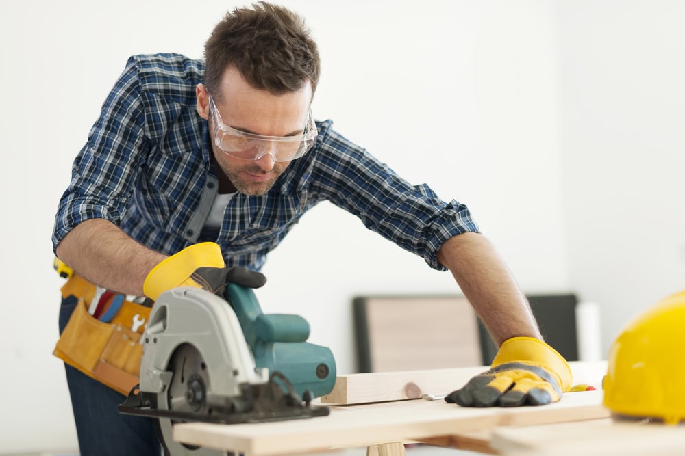 Man using a circular saw on wood at a construction site.