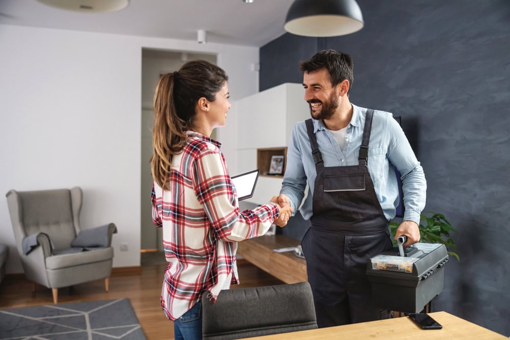 Friendly handyman shaking hands with happy female client indoors.