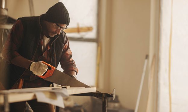 Man using handsaw on wood at construction site.