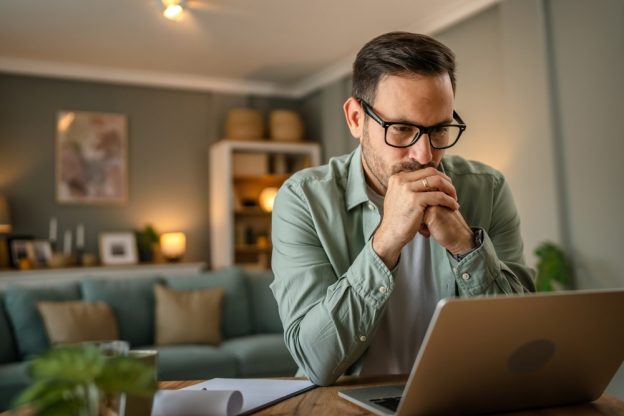 Professional man contemplating contractor licensing requirements on his laptop at home.
