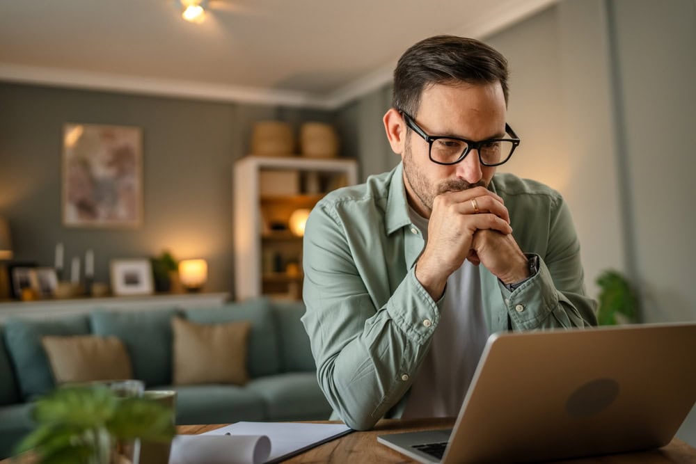 Professional man contemplating contractor licensing requirements on his laptop at home.