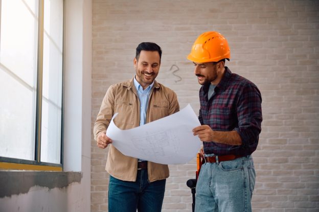 A contractor and a construction worker reviewing blueprints inside a building.