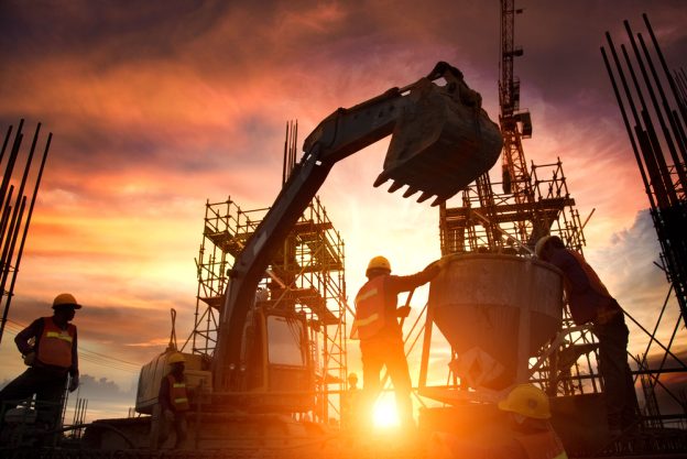 Construction site with workers pouring concrete at sunset, illustrating skilled contractor work and project management.