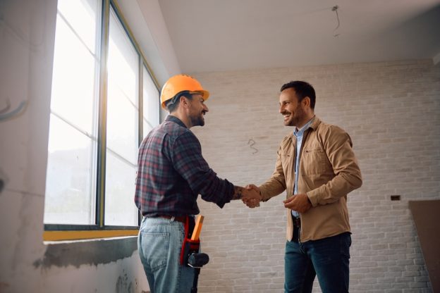Two contractors shake hands inside a room under construction, symbolizing partnership and agreement in the building industry.