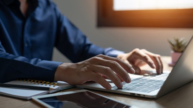 Professional person typing on a laptop, working at a desk with a notebook and plant, symbolizing contractor licensing and business setup.