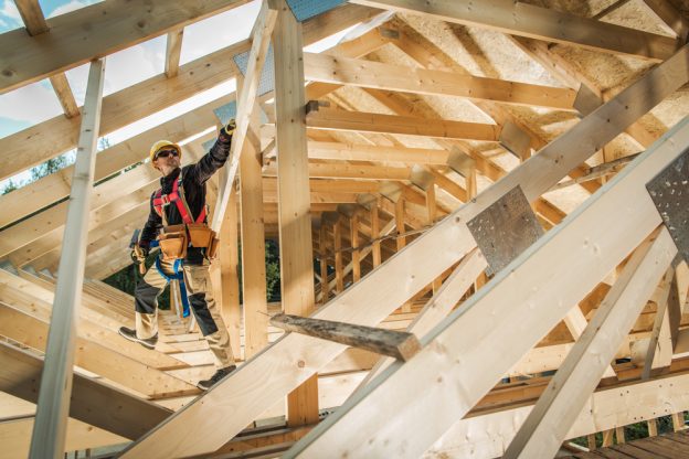 Construction worker inspecting wooden roof framework during residential building process.