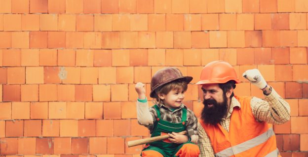 Construction worker and young boy celebrating victory on building site, safety gear, teamwork, profession, success.