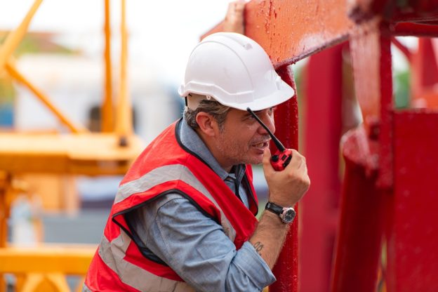 Safe construction worker with a hard hat and safety vest inspecting a red steel beam on a construction site.