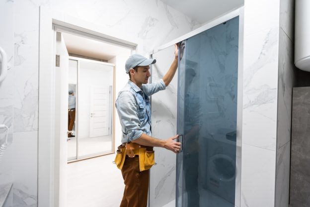 Professional contractor installing a glass shower door in a modern bathroom.