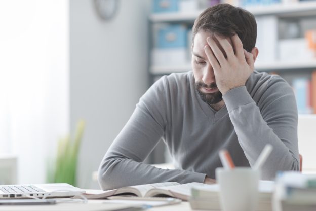 Frustrated man reading a book at his desk in an office setting, worried about contractor licensing and certification requirements.