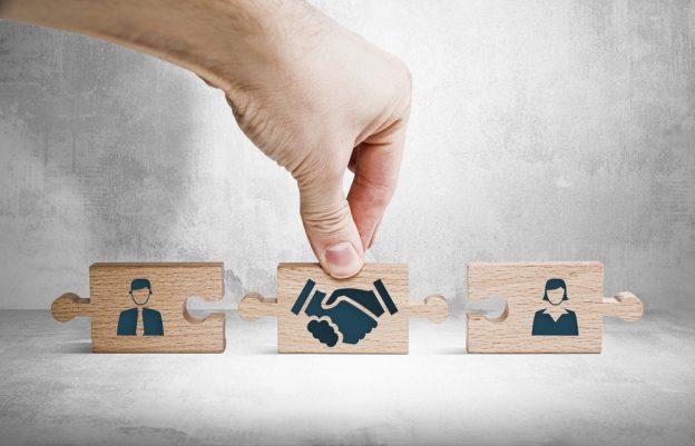 Reliable handshake icon on wooden puzzle pieces representing partnership and collaboration in the construction industry.