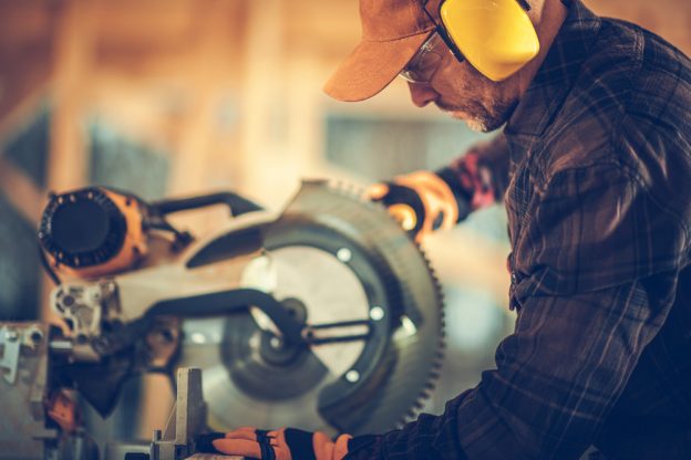 Precise electrician cutting a piece of wood in a workshop, focusing on safety and craftsmanship.