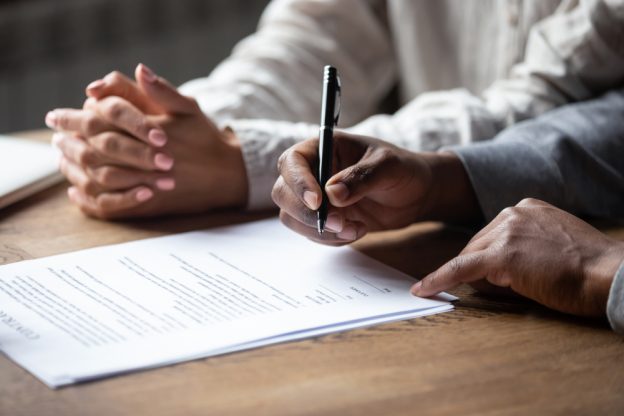 Hands signing a contract at a desk, representing contractor licensing and certification processes.