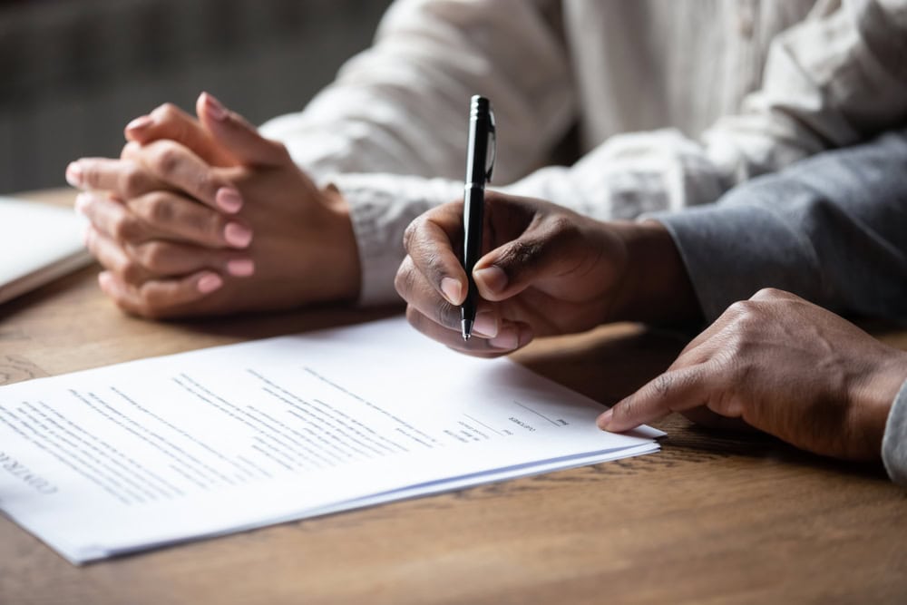 Hands signing a contract at a desk, representing contractor licensing and certification processes.