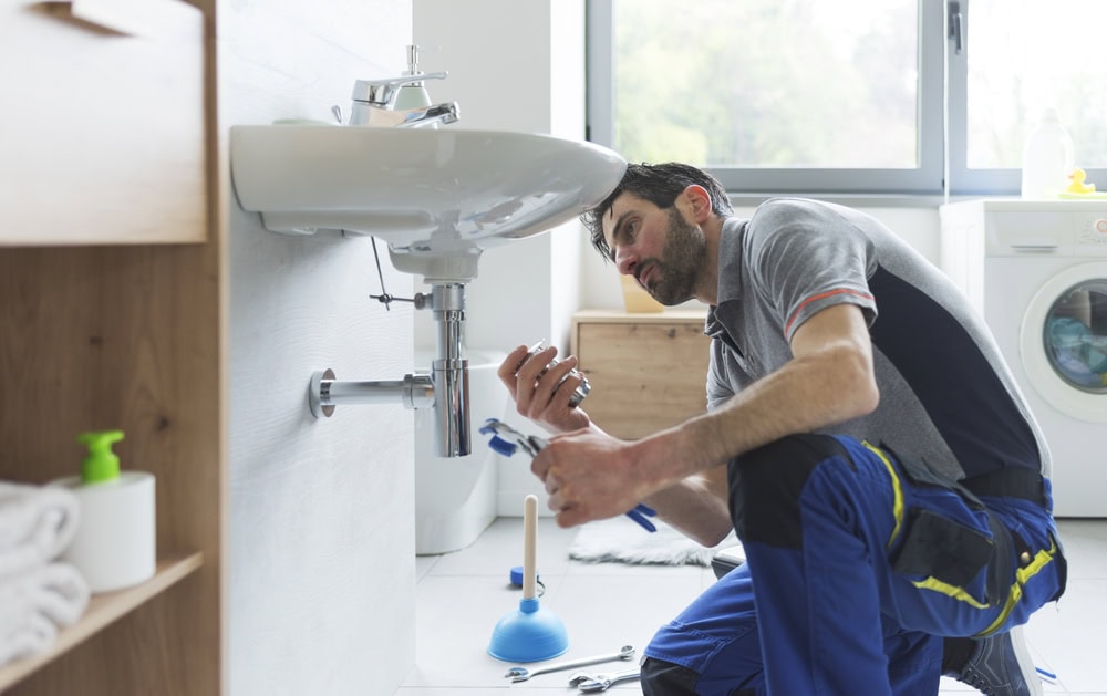 A skilled plumber repairing a bathroom sink with tools in a bright, modern laundry room.