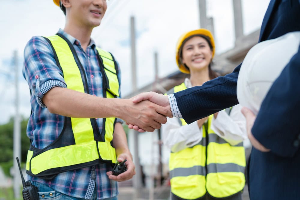 Contractors shaking hands on a construction site, emphasizing professionalism and project collaboration.