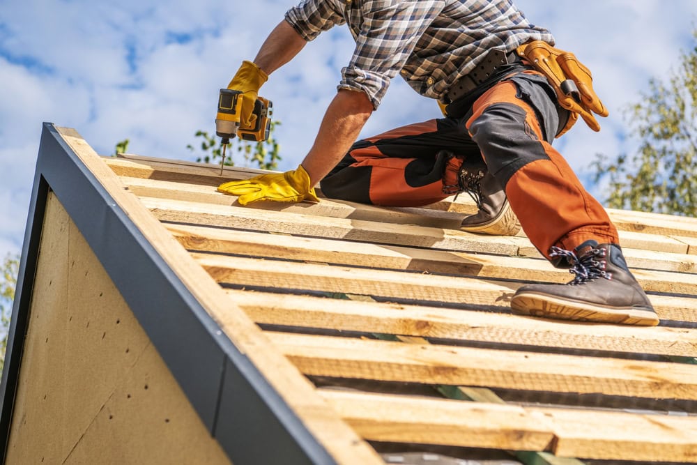 Construction worker installing roof shingles on a wooden roof deck during daytime.