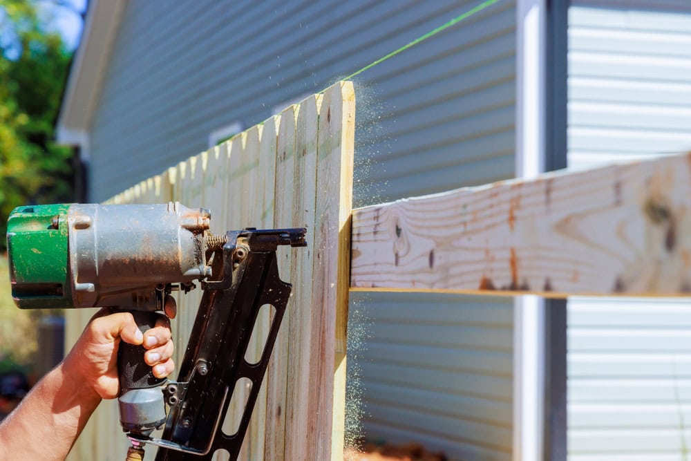 Heavy-duty nail gun fastening wooden fence panels during DIY construction project.