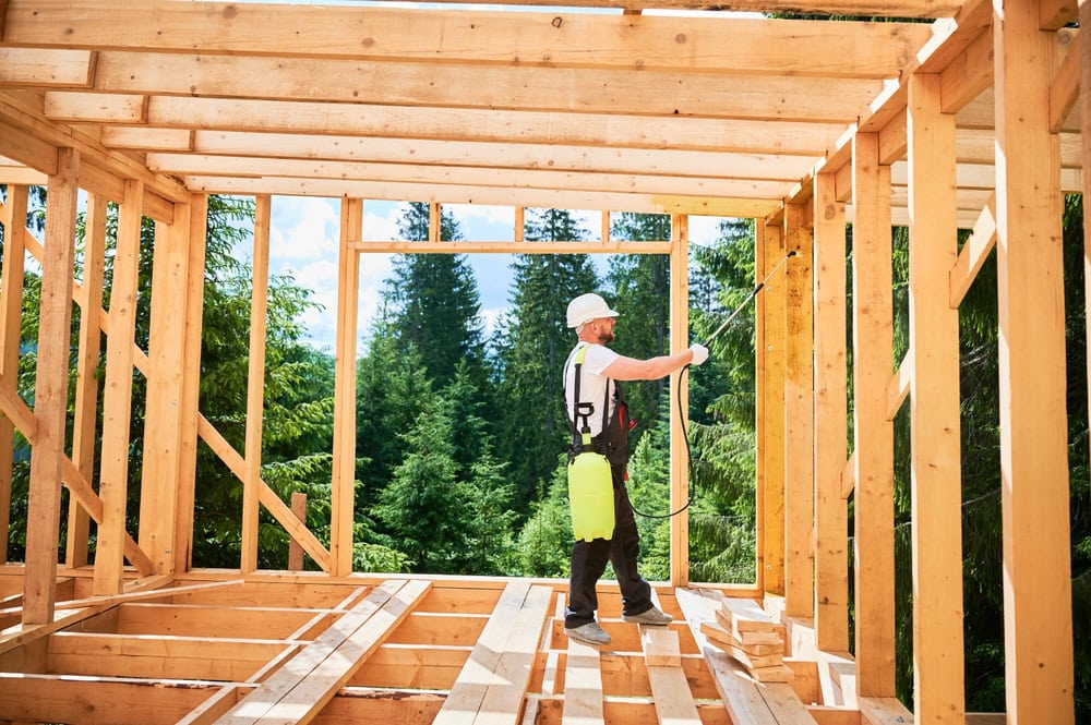 A construction worker inspecting wooden framing on a house under construction in a forested area.