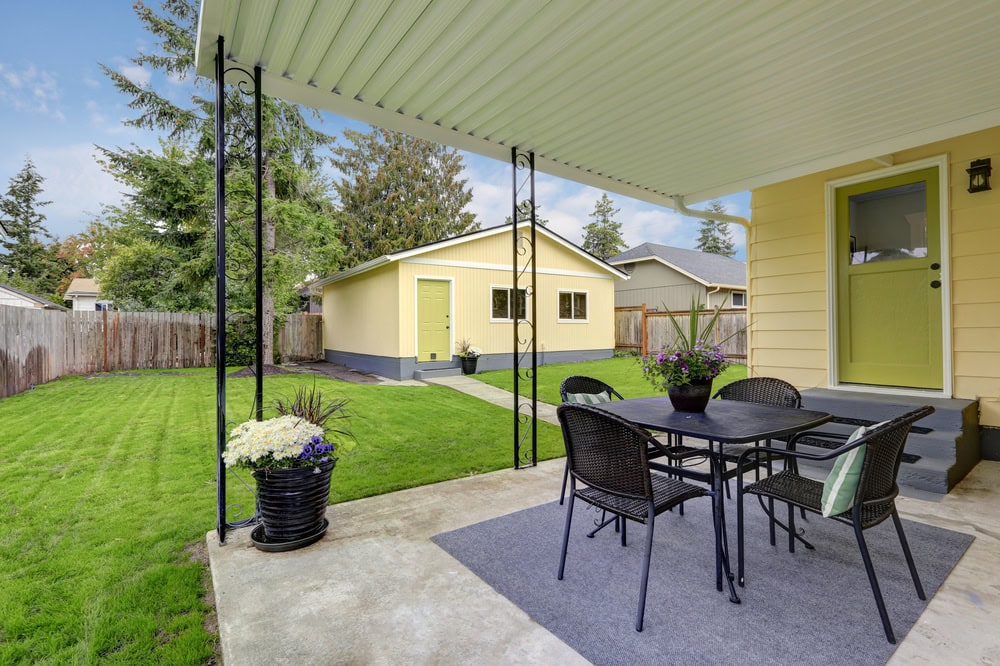 Bright yellow backyard house with a covered patio, outdoor dining area, and lush green lawn, showcasing home improvement and outdoor living solutions.