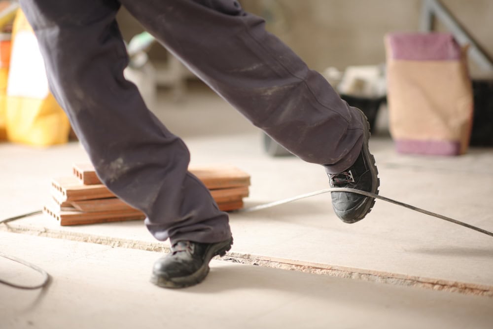 Flooring installation worker bending over with safety shoes on, working on a construction site.