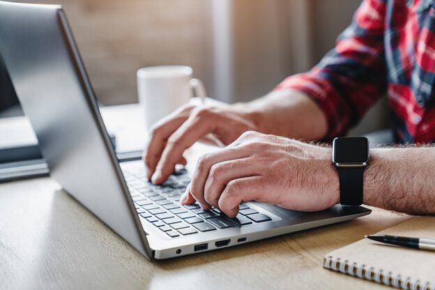 Male hands typing on a laptop keyboard with a smartwatch on the wrist, education or construction licensing preparations, modern technology use, workspace scene, professional environment, making a contractor.