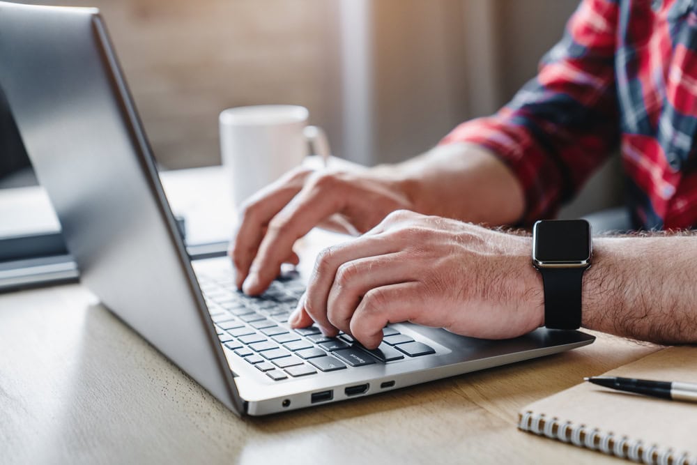 Male hands typing on a laptop keyboard with a smartwatch on the wrist, education or construction licensing preparations, modern technology use, workspace scene, professional environment, making a contractor.