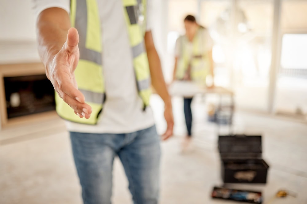 Able and confident contractor giving handshake at construction site, demonstrating professionalism and trustworthiness.