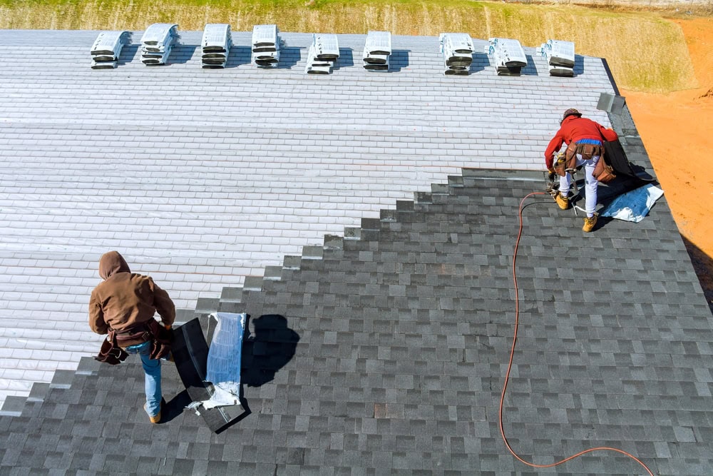 Roofing contractors installing asphalt shingles on a roof, demonstrating construction expertise and safety procedures.