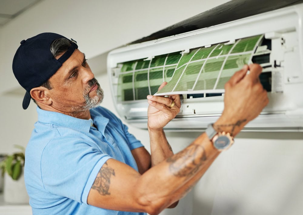 Professional HVAC technician inspecting and replacing air conditioner filters on wall-mounted unit.