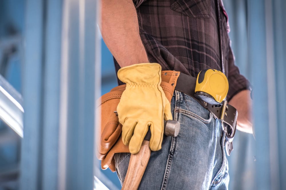 Worker with yellow glove holding hammer at construction site.